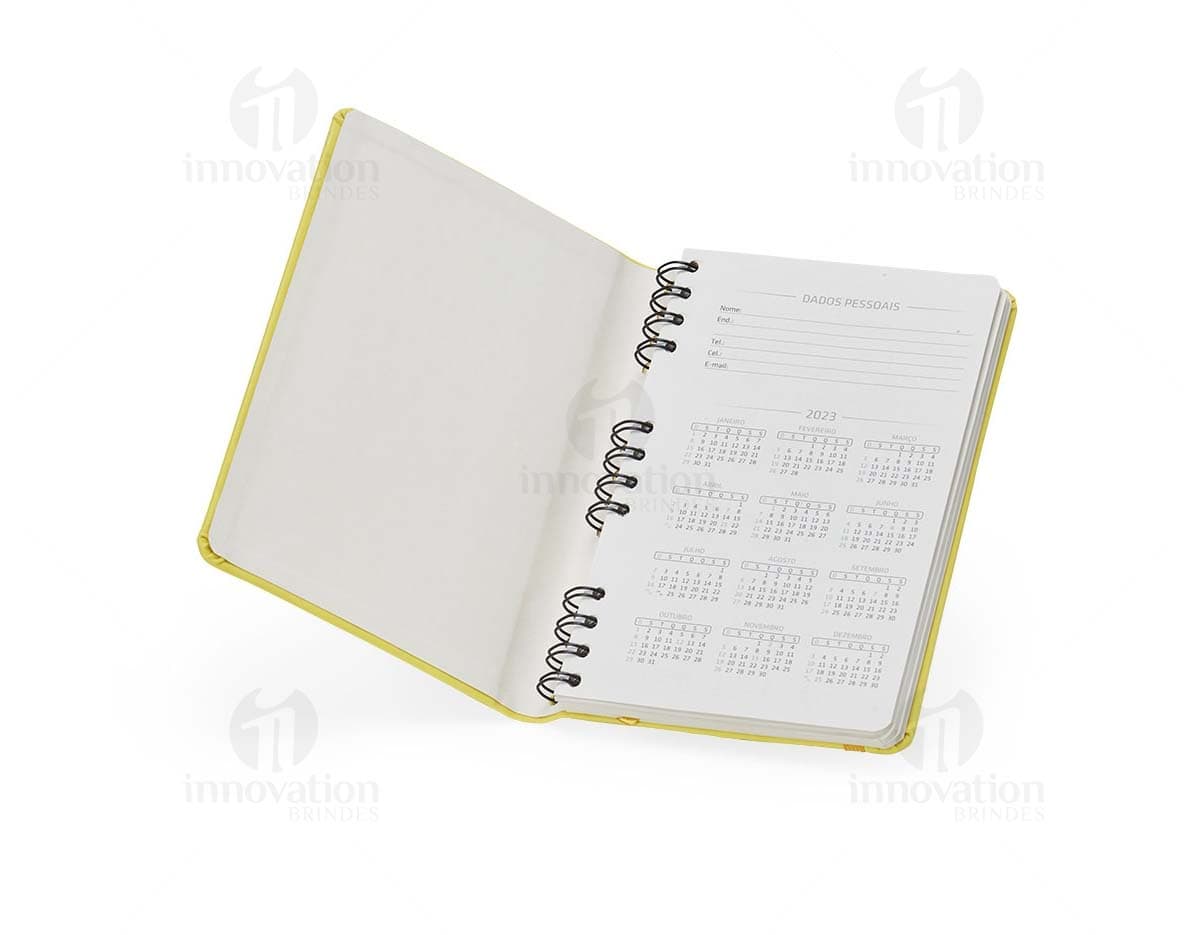 Caderneta Emborrachada com Wire-o em amarelo, design de quadro adesivo vazio em um notebook aberto, com papel em branco e um envelope de papel à direita, sobre fundo liso e limpo.
