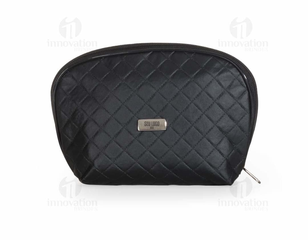 Necessaire de couro marrom com matelassê, estilo vintage, com fecho de fivela e alça de metal. O objeto está aberto, mostrando o interior vazio e forrado de papel. O design é elegante e fashion, com detalhes em couro e metal brilhante.
