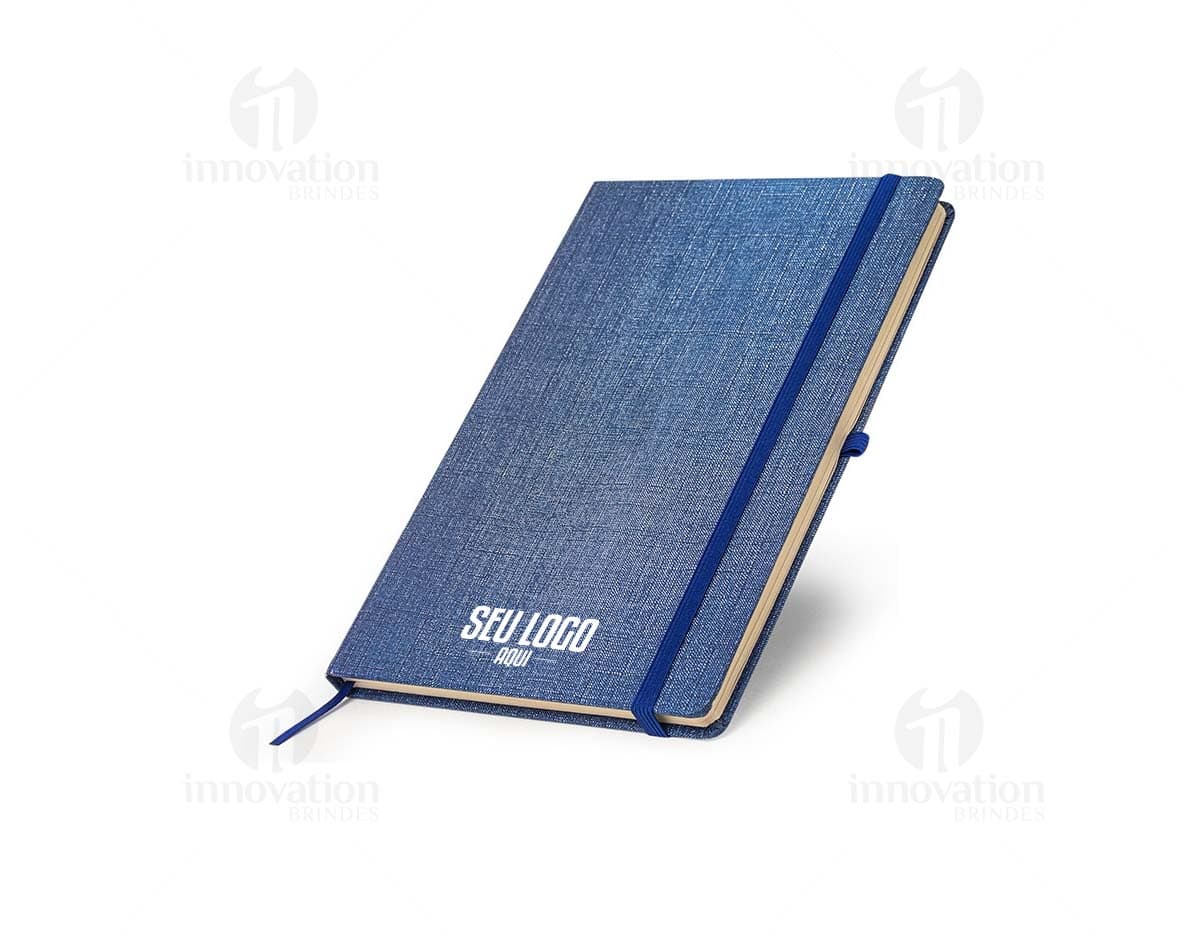 Caderneta A5 em papel texturizado antigo, com capa de tecido vintage em tom de marrom desgastado. O design é grunge e possui um padrão decorativo. O material é de fibra de algodão áspera, com uma superfície em canvas. Na capa, há um detalhe de costura em linha preta. O interior está em branco, com páginas vazias.