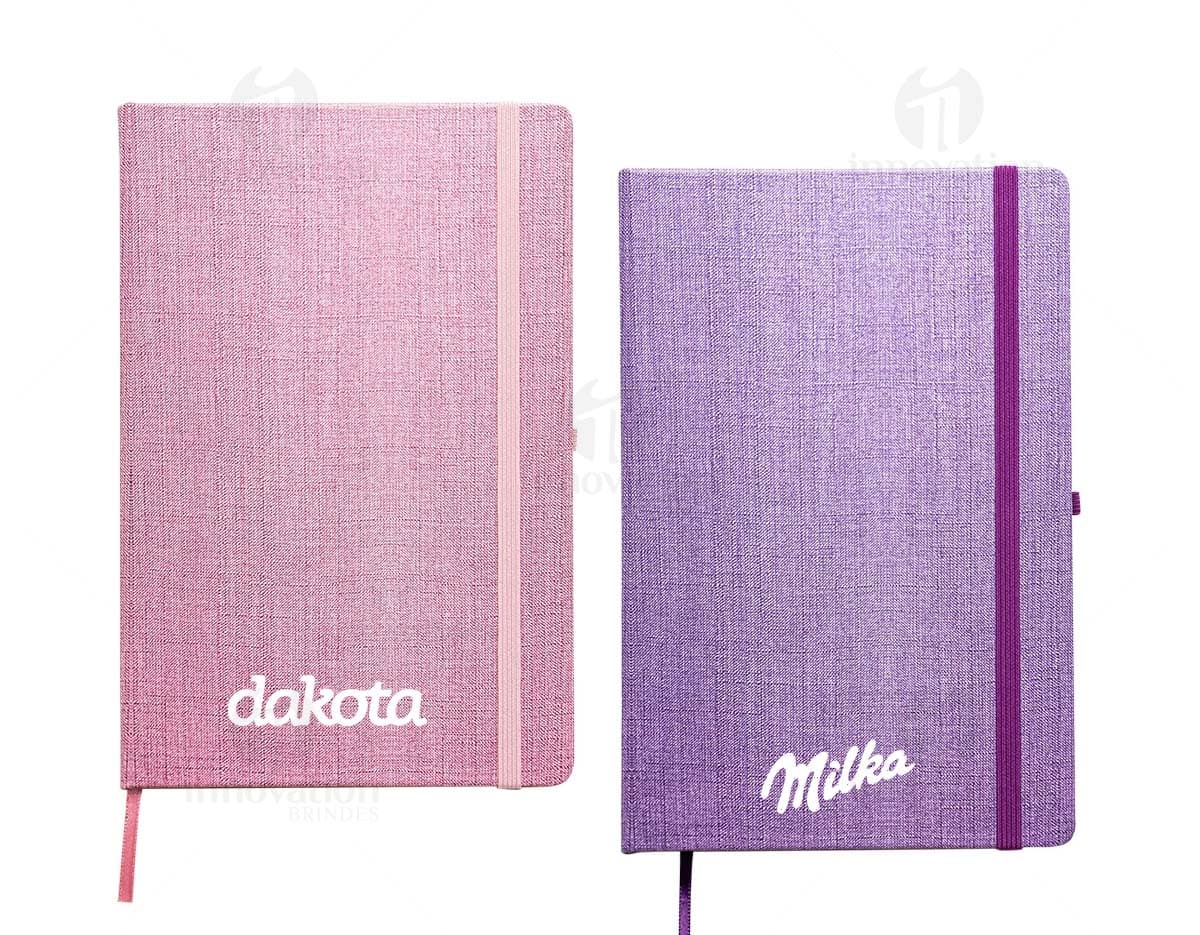 Caderneta A5 em papel texturizado antigo, com capa de tecido vintage em tom de marrom desgastado. O design é grunge e possui um padrão decorativo. O material é de fibra de algodão áspera, com uma superfície em canvas. Na capa, há um detalhe de costura em linha preta. O interior está em branco, com páginas vazias.
