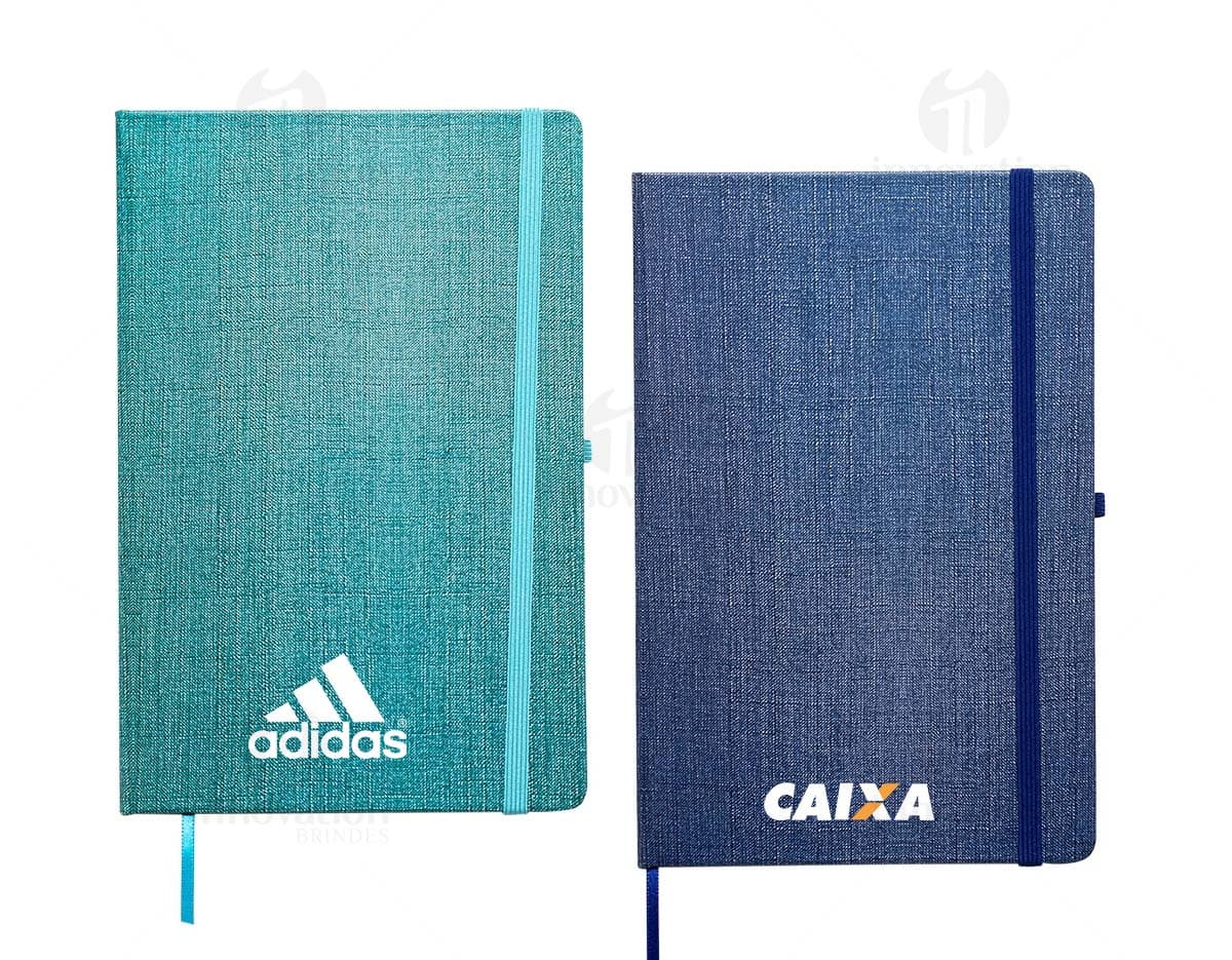Caderneta A5 em papel texturizado antigo, com capa de tecido vintage em tom de marrom desgastado. O design é grunge e possui um padrão decorativo. O material é de fibra de algodão áspera, com uma superfície em canvas. Na capa, há um detalhe de costura em linha preta. O interior está em branco, com páginas vazias.
