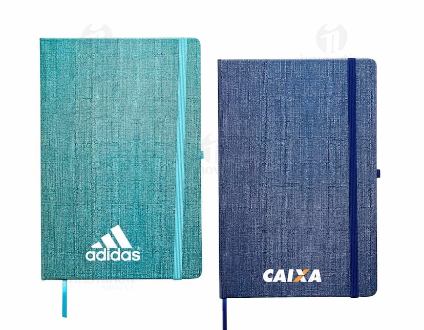 Caderneta A5 em papel texturizado antigo, com capa de tecido vintage em tom de marrom desgastado. O design é grunge e possui um padrão decorativo. O material é de fibra de algodão áspera, com uma superfície em canvas. Na capa, há um detalhe de costura em linha preta. O interior está em branco, com páginas vazias.