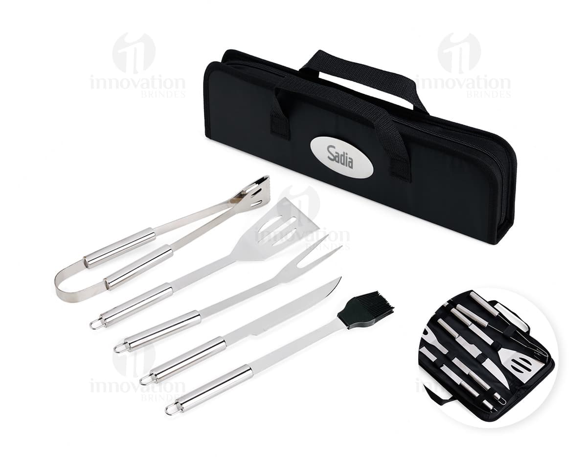 Kit Churrasco 5 Peças - Conjunto contendo faca, garfo, pinça, espátula e escova para churrasco em fundo de madeira.