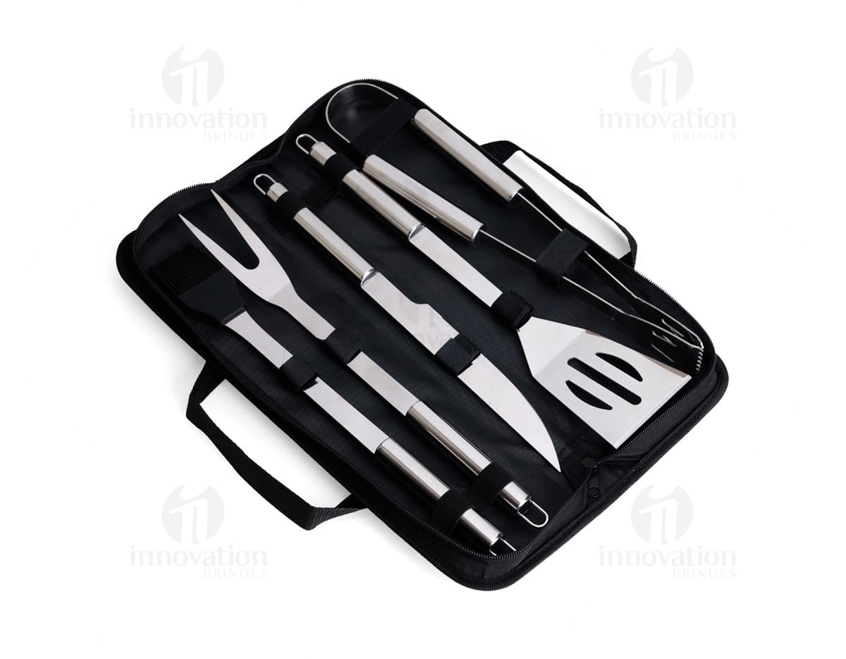 Kit Churrasco 5 Peças - Conjunto contendo faca, garfo, pinça, espátula e escova para churrasco em fundo de madeira.
