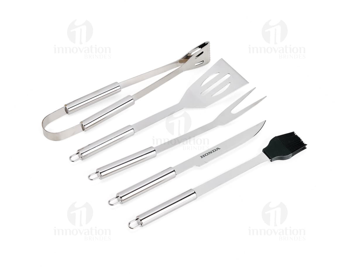 Kit Churrasco 5 Peças - Conjunto contendo faca, garfo, pinça, espátula e escova para churrasco em fundo de madeira.