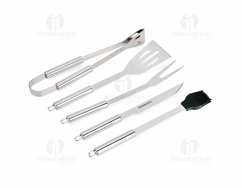 Kit Churrasco 5 Peças - Conjunto contendo faca, garfo, pinça, espátula e escova para churrasco em fundo de madeira.