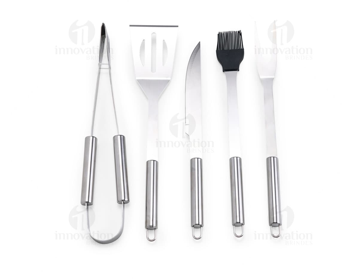 Kit Churrasco 5 Peças - Conjunto contendo faca, garfo, pinça, espátula e escova para churrasco em fundo de madeira.