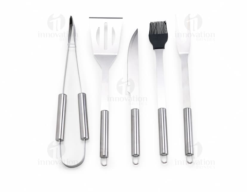 Kit Churrasco 5 Peças - Conjunto contendo faca, garfo, pinça, espátula e escova para churrasco em fundo de madeira.