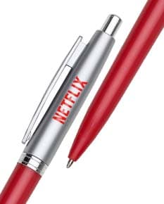 Caneta plástica azul com tampa transparente ao lado de um caderno em uma mesa de madeira.