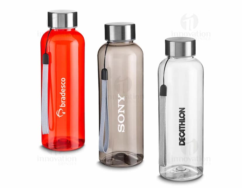 Garrafa plástica de 500ml em cor amarela, com tampa de metal e design transparente. A garrafa contém líquido e está próxima de um frasco de cremes e um frasco de perfume. A imagem mostra objetos de cuidados de higiene e beleza no banheiro.