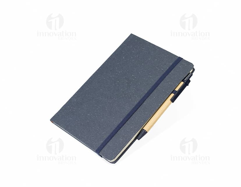 Caderneta de fibra de arroz com caneta em fundo branco. O caderno é marrom claro e possui detalhes em preto na capa. A caneta é de cor azul e está ao lado da caderneta.