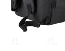 Homem de terno preto e pasta executiva, segurando uma mochila preta nas costas, em um ambiente corporativo.