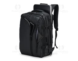 A smiling, well-dressed businessman holding a black leather backpack. He is standing in a studio and looks happy and