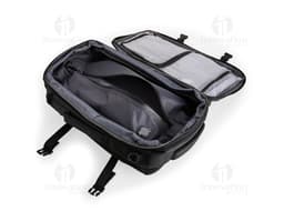 A smiling, well-dressed businessman holding a black leather backpack. He is standing in a studio and looks happy and