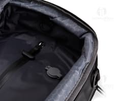 A smiling, well-dressed businessman holding a black leather backpack. He is standing in a studio and looks happy and