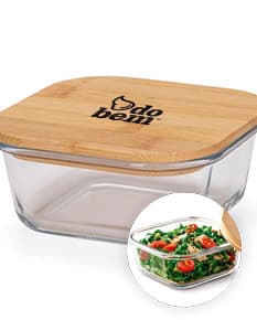 Marmita de vidro de 400ml contendo uma refeição saudável e gourmet, composta por diversos alimentos frescos e coloridos, disposta sobre uma mesa de cozinha de madeira.