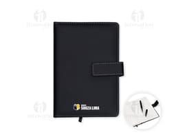 Conjunto executivo composto por notebook preto e bloco de notas de couro preto sobre uma mesa de escritório. O notebook está