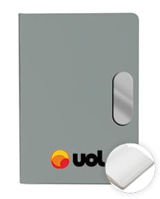 Caderno em PU com placa em metal, objeto digital com design moderno e espaço vazio para etiqueta. Aparece em um ambiente de escritório com equipamentos tecnológicos, como computador, mouse e teclado, além de uma xícara de plástico e um dispenser de papel. A imagem é renderizada em 3D, com um toque de brilho e reflexão, representando um conceito de negócios e comunicação.