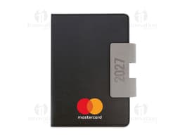 Notebook preto aberto, com teclado e tela exibindo ícones e botões. Ao lado, uma agenda A5 com capa dura em PU, destacando-se