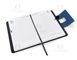 Notebook preto aberto, com teclado e tela exibindo ícones e botões. Ao lado, uma agenda A5 com capa dura em PU, destacando-se