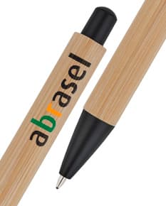 Caneta esferográfica em bambu de cor preta e detalhes em prata, sobre um papel em branco e um caderno de anotações. O objeto está posicionado de forma fechada, mostrando o design elegante e a combinação de materiais como metal e madeira.