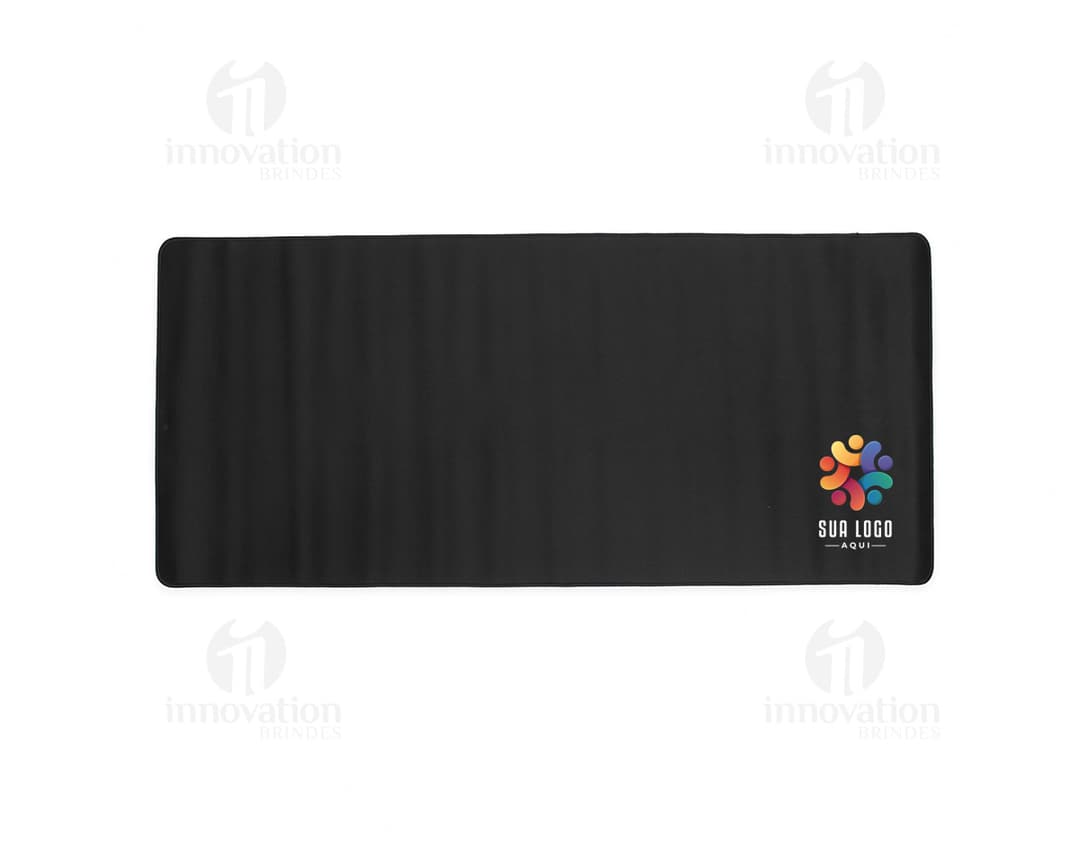 Desk pad em poliéster preto sobre uma mesa de madeira, com caneta, celular e notebook ao lado.