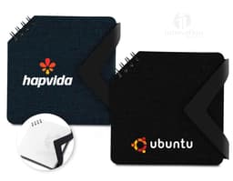 Black leather mini notebook open on an office desk, next to a laptop and various electronic devices. It contains blank pages