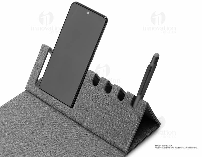 Mouse pad de couro marrom aberto em cima de uma mesa de escritório, ao redor estão um notebook preto, uma bolsa de couro, chaves, um cartão de crédito, uma carteira, um bloco de notas, um teclado preto e um mouse preto.