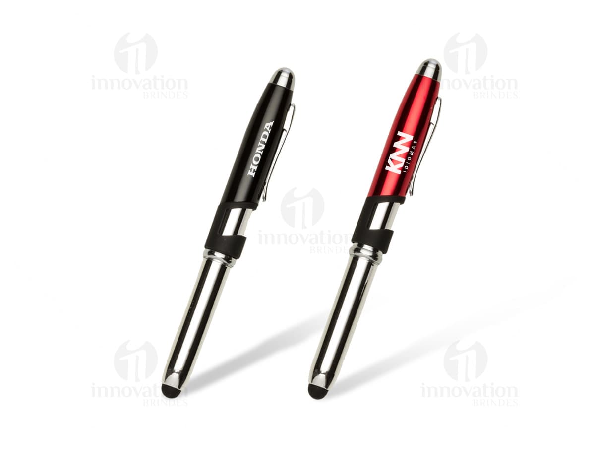 Mini caneta touch com suporte para celular em tom de prateado. Está sobre uma mesa de madeira clara, ao lado de um smartphone preto.