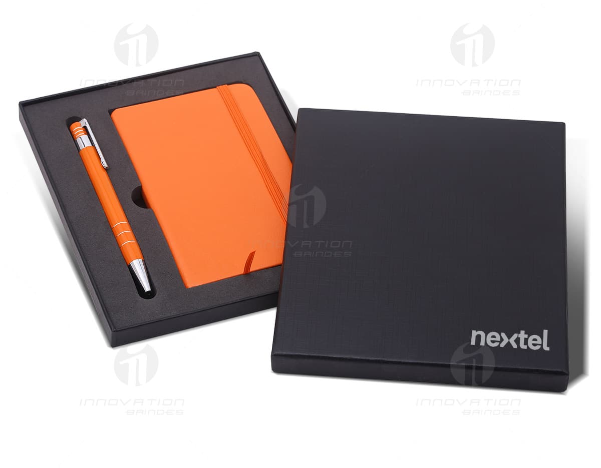 Kit executivo contendo dois itens. O primeiro é um elegante estojo de couro preto com zíper e alça. O segundo item é uma caneta esferográfica prateada com detalhes em dourado e marcação a laser da logomarca da empresa. Kit executivo contendo dois itens. O primeiro é um elegante estojo de couro preto com zíper e alça. O segundo item é uma caneta esferográfica prateada com detalhes em dourado e marcação a laser da logomarca da empresa.
