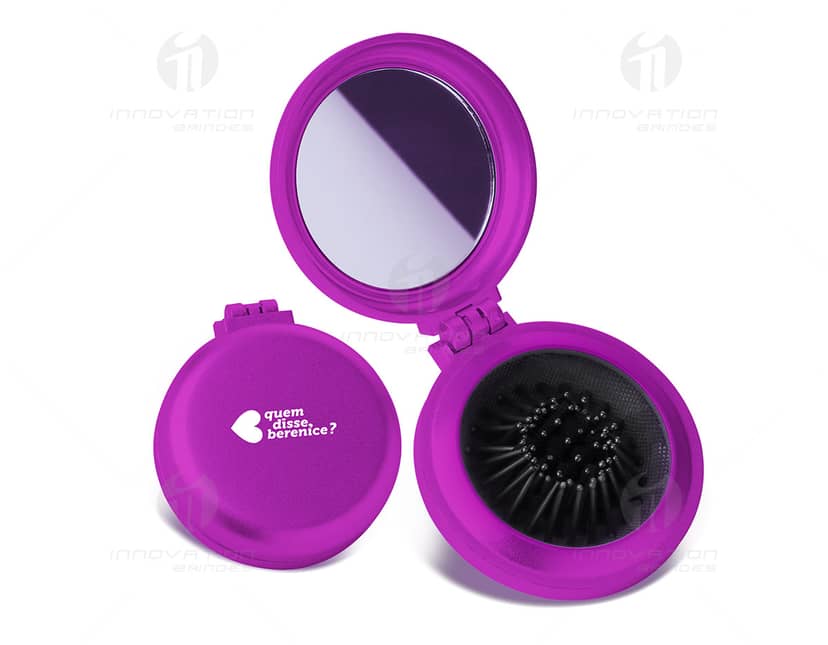Espelho de bolsa roxo, redondo e brilhante com escova de maquiagem acoplada. O design inclui um disco vazio e símbolos coloridos, em metal e plástico. Ideal para retoques rápidos durante o dia.