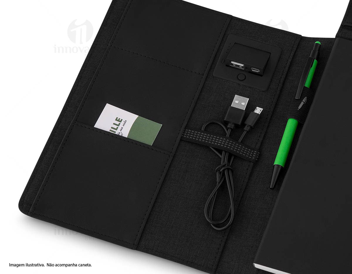 Bloco de anotações com powerbank preto sobre uma mesa de madeira, com caneta ao lado e cabo de carregamento visível. Bloco de anotações com powerbank preto sobre uma mesa de madeira, com caneta ao lado e cabo de carregamento visível.