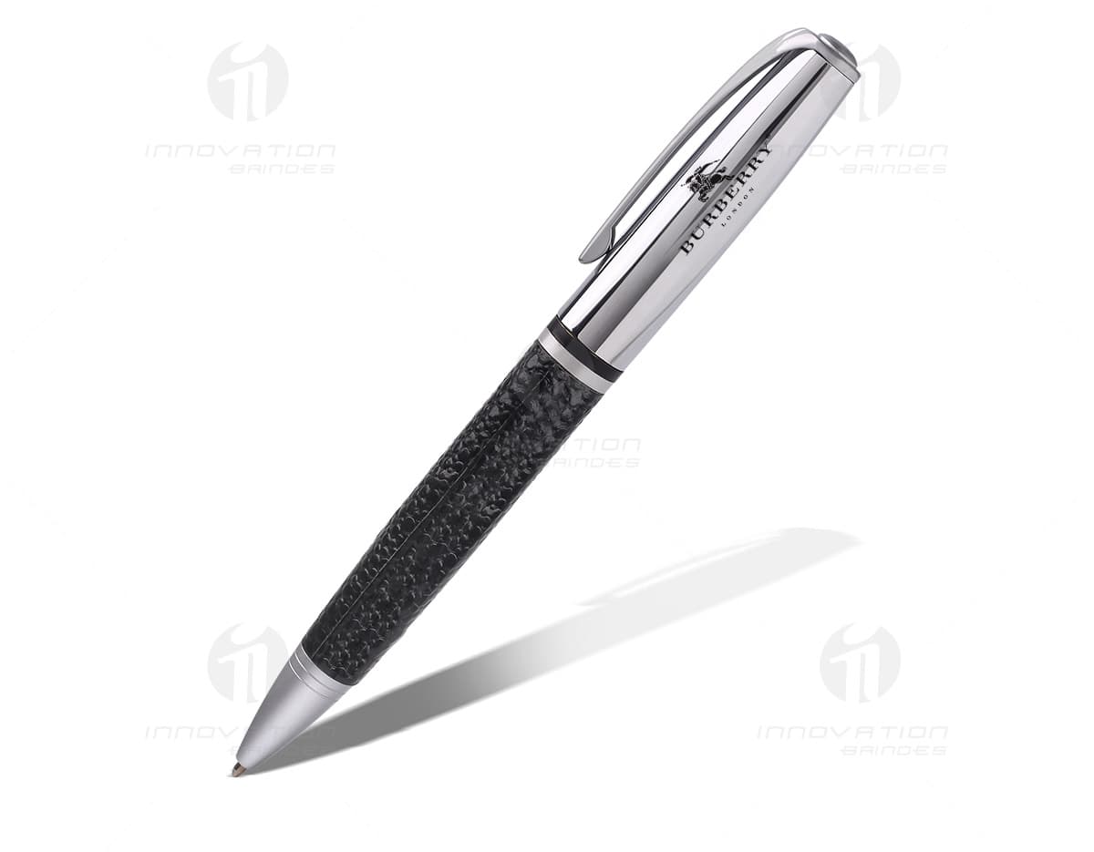 Caneta de metal na cor prata, com detalhes em preto e acabamento acetinado. O produto está sobre uma mesa de madeira escura. Caneta de metal na cor prata, com detalhes em preto e acabamento acetinado. O produto está sobre uma mesa de madeira escura.