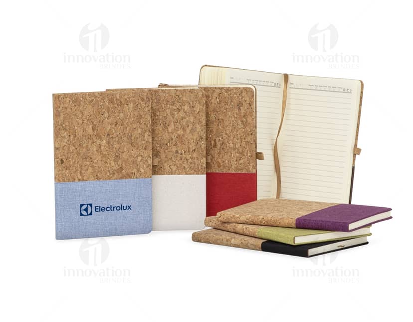 Caderneta em Cortiça com capa marrom claro e elástico para fechamento, sobre fundo branco. Páginas em branco com detalhes em dourado.